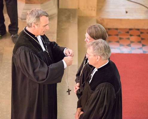 Oberkirchenrat Michael Martin legt den neuen Direktoren das Amtskreuz um. © MEW/Ermann