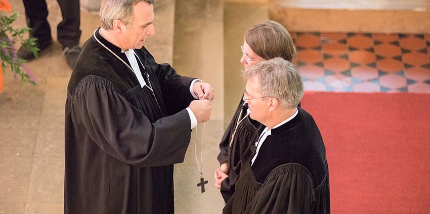 Oberkirchenrat Michael Martin legt den neuen Direktoren das Amtskreuz um. © MEW/Ermann